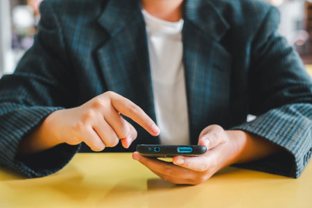 Close-up of a person using a smartphone, wearing a plaid blazer, and touching the screen. Casual and modern setting.の写真素材