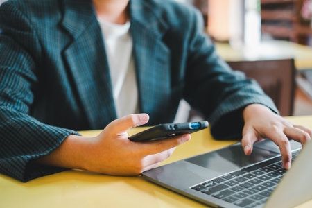 Close-up of a business professional using a smartphone and laptop, highlighting modern technology in a professional environment.の写真素材