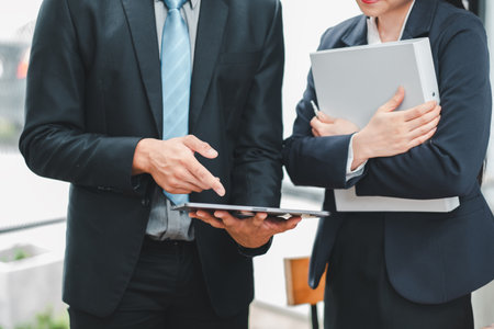 Two business professionals in formal attire discussing work on a tablet in a modern office environment.の写真素材