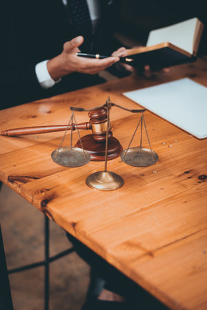 A lawyer in a suit discusses legal matters with a client in an office, with a gavel and scales of justice prominently displayed on a wooden desk.の写真素材