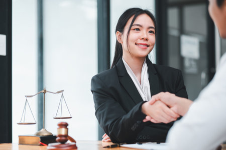Confident businesswoman in a suit shaking hands with a client, symbolizing successful negotiation or agreement in a professional office environment.の写真素材