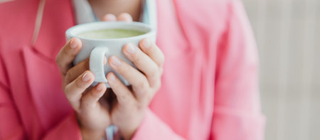 Close-up of a woman in a pink blazer holding a cup of green tea, creating a warm and cozy atmosphere.の写真素材