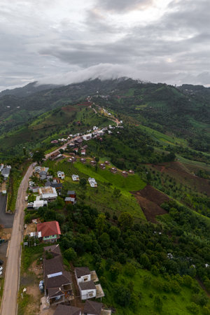 Stunning aerial shot of a picturesque village nestled in lush green hills under a cloudy sky.の写真素材