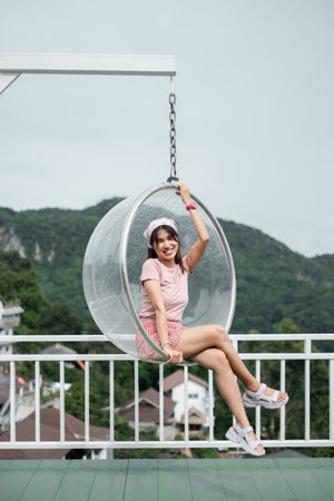 ** Smiling woman sitting in a transparent hanging chair with lush green mountains in the background, enjoying a peaceful day outdoors.

**の写真素材