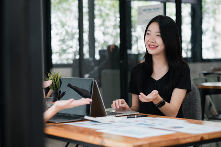 A young woman in a modern office setting, engaging in a business meeting with a colleague, using a...