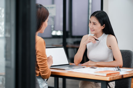 Two women discussing business strategies in a contemporary office setting, emphasizing teamwork and collaboration.の写真素材