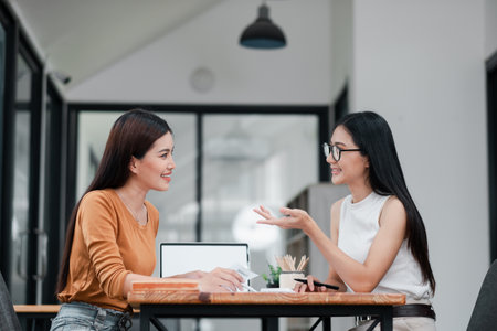Two women discussing business strategies in a contemporary office environment, showcasing teamwork and collaboration.の写真素材