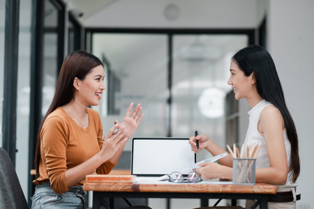 Two women having a productive business discussion in a contemporary office setting, showcasing teamwork and collaboration.の写真素材