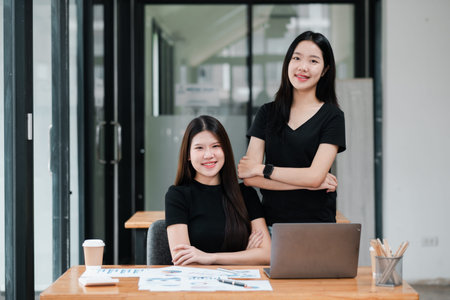 Two professional women in a contemporary office setting, working together on a project with a laptop and documents.の写真素材