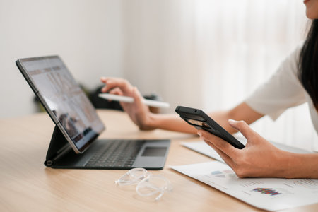 Professional woman using smartphone and tablet at a desk, showcasing multitasking in a modern office...