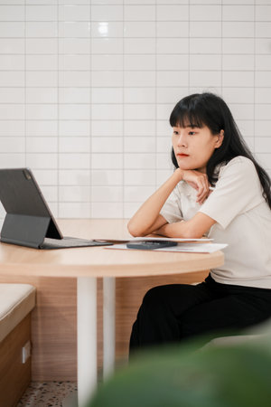 Focused woman using a tablet in a stylish cafe setting, featuring a modern interior with white tiles and wooden furniture.の写真素材