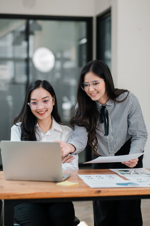 Two women working together in a contemporary office, discussing ideas and using a laptop.の写真素材