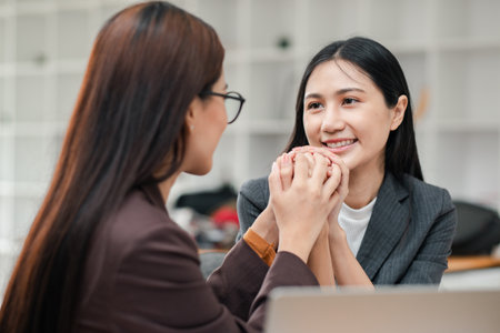Two businesswomen in a modern office, sharing a supportive moment, highlighting teamwork and professional relationships.の写真素材