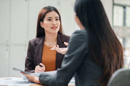 Two businesswomen engaged in a professional meeting, discussing documents in a modern office environment.の写真素材