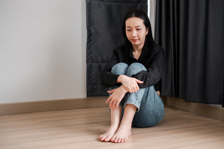 A young woman sits on the floor, head down, in a moment of reflection and solitude, surrounded by soft natural light.の写真素材