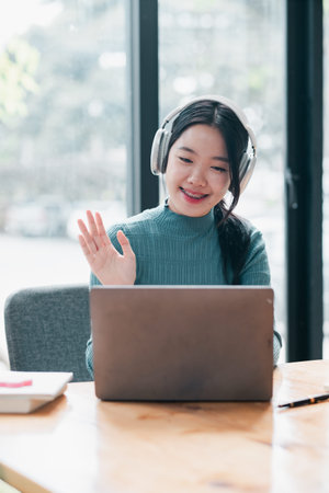 Smiling woman using laptop and headphones for video call in a bright office environment.