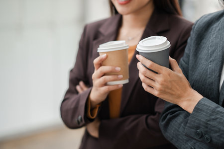 Close-up of two business professionals holding coffee cups during a break in an urban environment.の写真素材