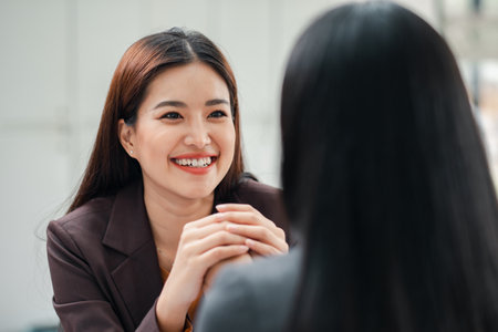 Two women engaged in a friendly business meeting, showcasing professional interaction and communication in a modern office environment.の写真素材