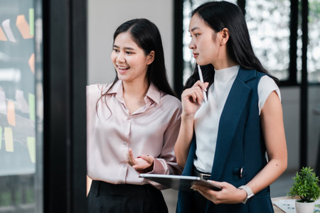 Two businesswomen discussing ideas in a contemporary office, using a tablet and sticky notes for brainstorming.の写真素材