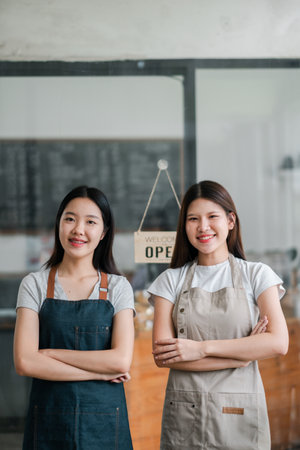 Two young female baristas in aprons standing confidently in front of a coffee shop, showcasing a welcoming atmosphere.の写真素材