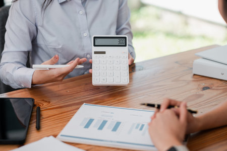 Professionals discussing financial data with a calculator and charts on a wooden table during a business meeting.の写真素材