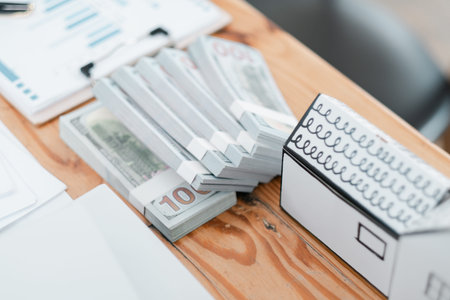 Close-up of stacks of cash and financial documents on a wooden desk, symbolizing finance and...