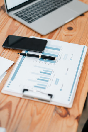 A modern office setup featuring a laptop, smartphone, and financial charts on a wooden desk, ideal for business and finance themes.の写真素材