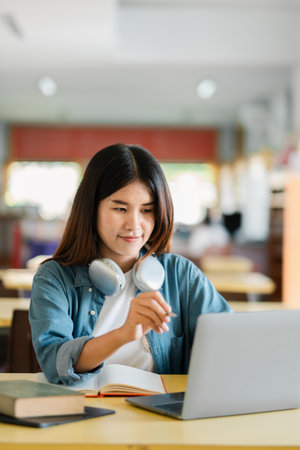 Young woman with headphones using a laptop in a cafe, focused on studying and online learning.の写真素材