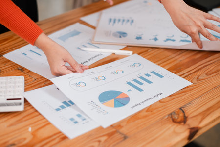 Close-up of hands reviewing financial charts and graphs on a wooden desk, showcasing teamwork and data analysis.の写真素材