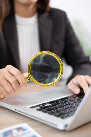 A business professional uses a magnifying glass to closely examine data on a laptop, symbolizing attention to detail and analysis.の写真素材