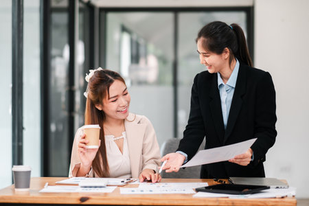 Two businesswomen discussing documents in a bright, modern office setting, fostering teamwork and collaboration.の写真素材