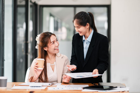 Two professional women discussing documents in a bright office, fostering teamwork and...