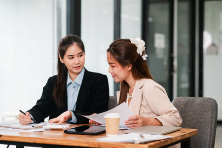 Two women in a business meeting discussing documents in a modern office environment, showcasing teamwork and collaboration.の写真素材