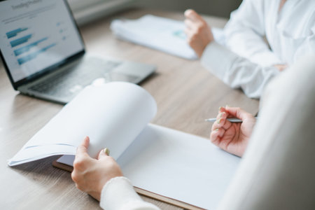 Professionals engaged in a business meeting, reviewing documents and analyzing data on a laptop in a...