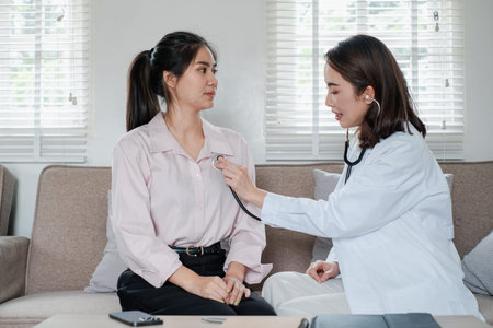 Female doctor using a stethoscope to examine a patient in a cozy living room environment,...