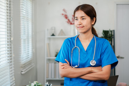 A healthcare professional in blue scrubs stands confidently with arms crossed in a modern medical office setting.の写真素材