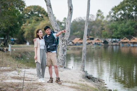 A couple stands by a serene lake, surrounded by trees and camping tents, enjoying the peaceful natural setting.の写真素材