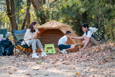 A family camping in the forest, enjoying nature with a tent and outdoor activities, surrounded by trees and leaves.の写真素材