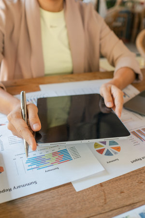 A business professional using a tablet to review financial charts and graphs on a wooden desk in an office environment.の写真素材
