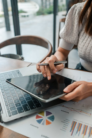 Professional woman using a tablet and laptop to review financial charts in a contemporary office...