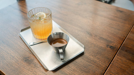 A citrus cocktail and espresso served on a metal tray, placed on a wooden table in a cozy cafe...