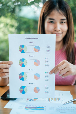 A professional woman holds a manufacturing report with pie charts, showcasing data analysis in a modern office environment.の写真素材