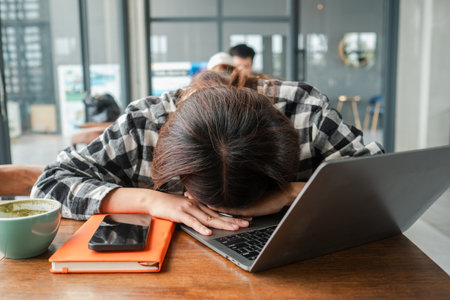 Tired woman with head on laptop in a cafe, showing stress and exhaustion from work.の写真素材