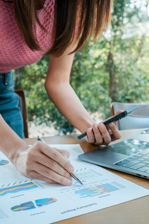 Professional woman reviewing financial charts with a laptop and smartphone, showcasing modern business analysis.の写真素材