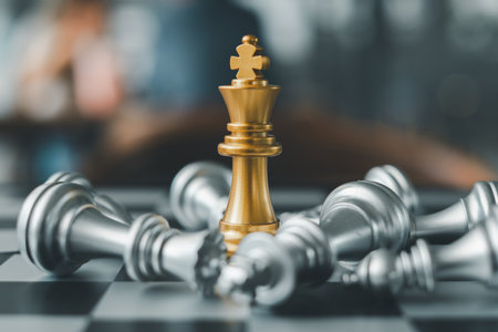 A golden chess king stands victorious on a chessboard surrounded by fallen pieces, symbolizing strategy and victory.の写真素材