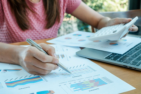 Close-up of a woman reviewing financial charts and using a calculator, highlighting business...