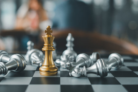 A golden chess king stands triumphantly on a chessboard surrounded by fallen silver pieces, symbolizing victory and strategy.の写真素材