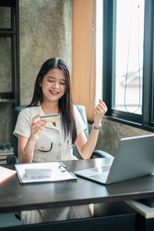 Smiling woman using a credit card for online shopping on a laptop in a stylish office environment.