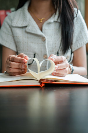 Close-up of a woman forming a heart shape with book pages, symbolizing love for reading and literature.の写真素材
