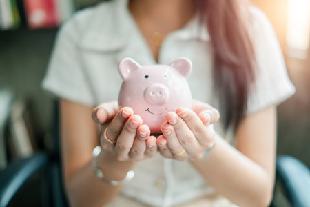 Close-up of a woman holding a pink piggy bank, representing savings, finance, and investment in a bright office environment.の写真素材